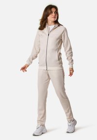 Beige zip-up sweatshirt with ribbed cuffs and hem, paired with matching beige sweatpants. Soft fabric, relaxed fit, no visible patterns.