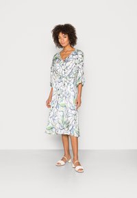 Vestido com padrão floral, decote em V, mangas de três quartos e um laço na cintura. As cores incluem verde, azul e branco. Combinado com sandálias leves.