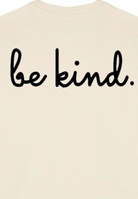 Krémová mikina s okrúhlym výstrihom a mäkkou textúrou, na zadnej strane so slovami "buď milý." v tučnom čiernom písme.