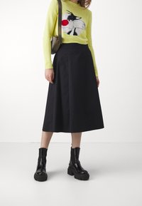 Żółty sweter z grafiką kreskówkową, czarna midi spódnica i czarne botki na masywnej podeszwie. Gładkie tekstury i kontrastujące kolory.