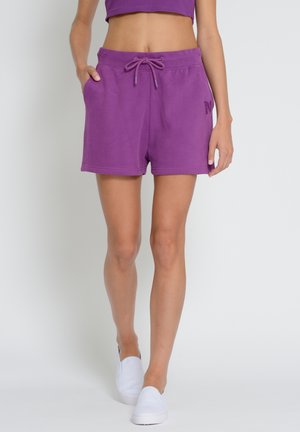 Purple cotton shorts with an elastic waistband, drawstring, and side pockets. Smooth texture, knee-length cut, featuring a small logo detail.