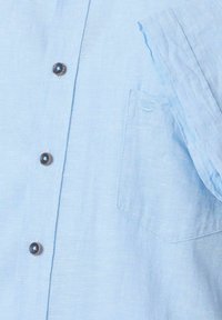 Lichtblauw overhemdd shirt van linnen, met een borstzak enbruine knopen. De stof heeft een gestructureerde, zachte uitstraling.