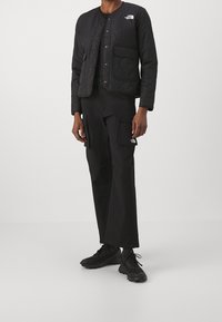 Černá prošívaná bunda s patentkami, obsahující náprsní kapsu. V kombinaci s černými cargo kalhotami a černými teniskami. Minimalistický a funkční design.