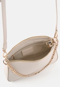 Helle beige Handtasche aus strukturiertem Leder, mit Reißverschluss, Innentasche und einem Akzent aus goldener Kette als Schulterriemen.