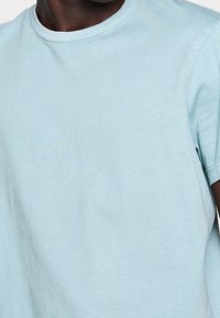 T-shirt bleu clair à manches courtes fabriqué en coton doux. Il présente un col rond classique et une coupe décontractée, sans motifs ni accents.