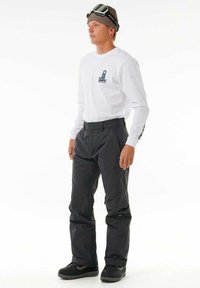 Witte lange mouwen top voor mannen met logo, gecombineerd met zwarte sneeuwbroeken. Heeft een relaxte pasvorm en een gladde textuur. Zwarte boots maken de outfit compleet.