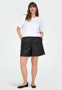 Bijela majica s malim mrljama, u kombinaciji s crnim kožnim hlačama viskog struka. Hlače imaju glatku teksturu i bočne džepove.