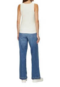 Wei�ßes ärmelloses Oberteil kombiniert mit blauen weiten Jeans. Die Jeans verfügen über ein klassisches Fünf-Taschen-Design und einen genähten Saum. Weiße Sneaker runden den Look ab.