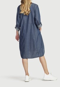 Denimklänning, knälång, med uppvikt ärm och rundad nederkant. Har en mjuk textur och en subtil sömdetalj på baksidan. Matchas med vita sneakers.