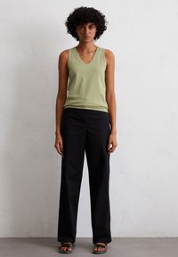 Light green sleeveless top with a V-neck design, paired with loose-fitting black trousers. Simple and smooth texture, casual look.
