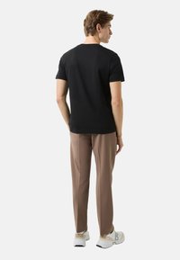 Černé tričko s krátkým rukávem, hnědé kalhoty na míru a bílé tenisky. Hladká tkanina. Minimalistický design s kulatým výstřihem.