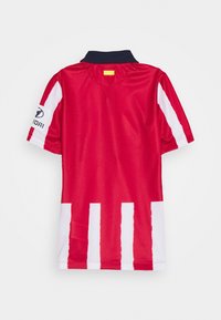Camisa de fútbol roja con un cuello negro, que presenta rayas verticales blancas a lo largo de los lados y un logo bordado en la manga.