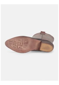 Braune Leder-Stiefelette mit runder Zehenform, minimalen Nähten und einer flachen Gummisohle, die eine geprägte Markenkennzeichnung auf der Unterseite aufweist.