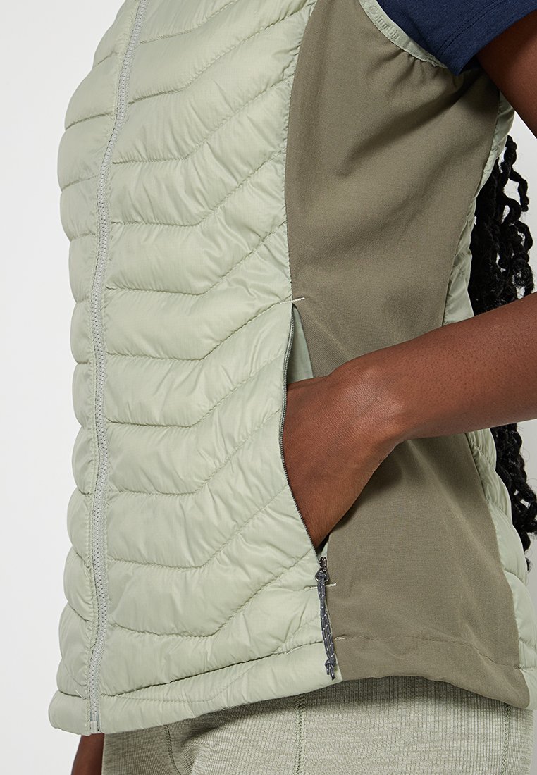 Gilet voluminoso di colore verde chiaro con texture trapuntata, dotato di un pannello laterale verde scuro e di una tasca laterale con chiusura a zip.