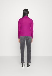 Dopasowany golf z długim rękawem w jaskrawym fioletowym kolorze, zestawiony z szarymi dżinsami. Tekstura jest gładka i elastyczna, z minimalistycznymi detalami wzorniczymi.