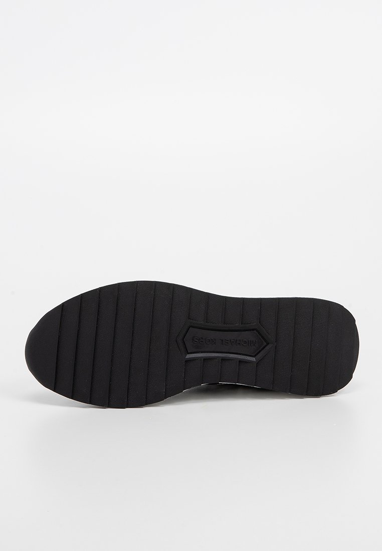 Suela de goma negra con surcos horizontales profundos para tracción. Presenta un logo hexagonal y un acabado liso sin adornos adicionales.