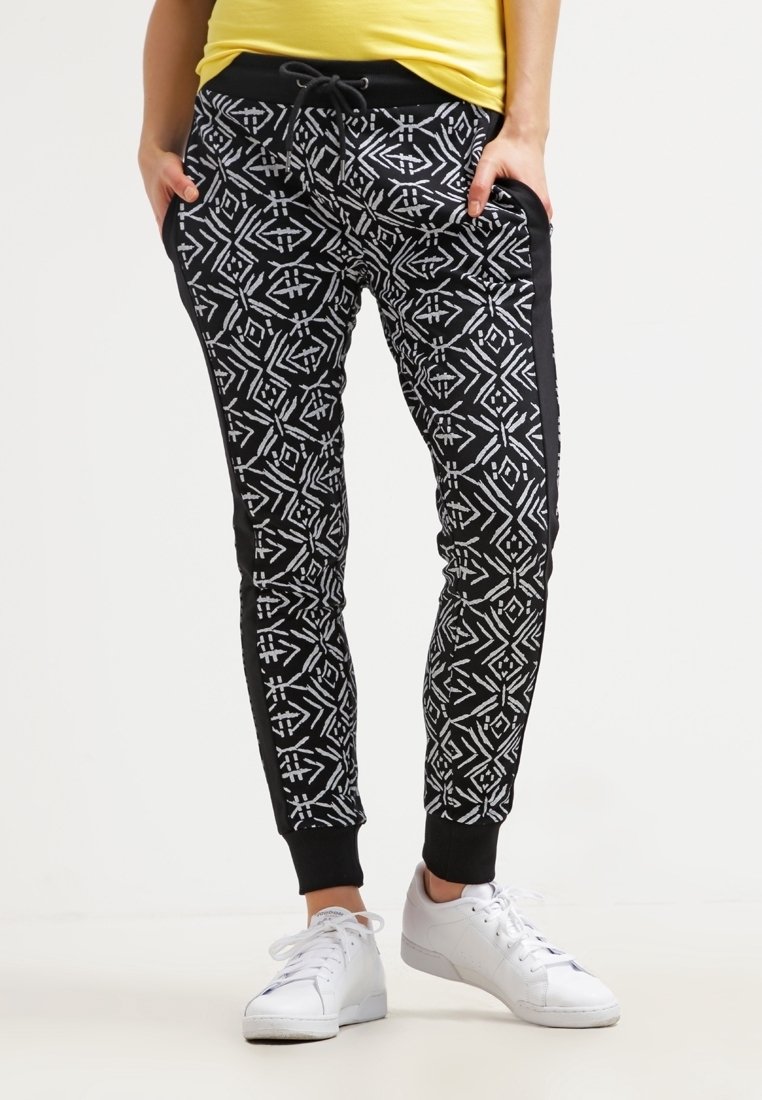Zwarte sweatpants met een wit geometrisch patroon, met zijzakken, een elastische tailleband en gebreide enkels. Gecombineerd met witte sneakers.