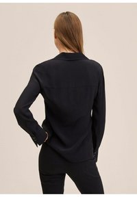Blouse noire à manches longues, col cranté et poignets boutonnés. Confectionnée dans un tissu lisse avec un design simple et ajusté.
