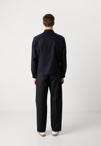 Casaco azul-marinho de mangas longas com colarinho, combinado com calças largas pretas e sapatos brancos. Textura suave e design simples.