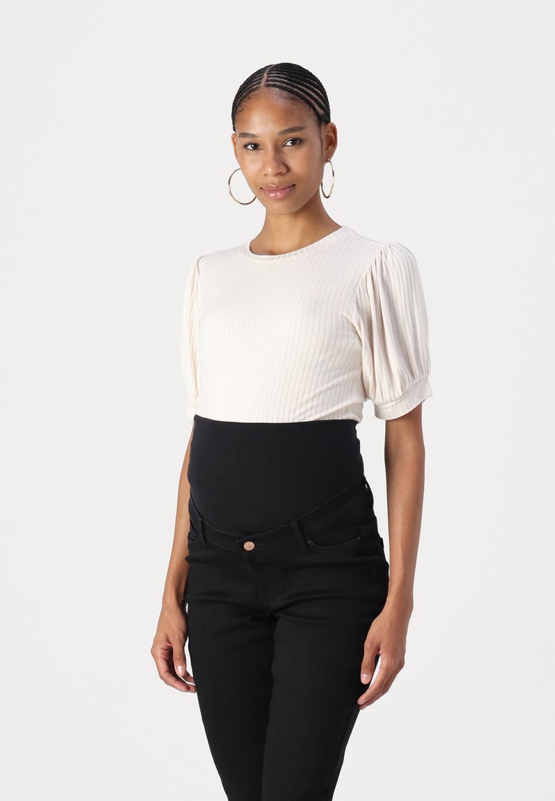 Top de canalé crema con mangas cortas abullonadas, combinado con jeans negros de cintura alta que tienen un cierre frontal de botones y bolsillos.