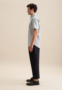 Camicia azzurro chiaro a maniche corte con colletto, abbinata a pantaloni blu scuro e scarpe nere. La camicia ha una singola tasca sul petto.