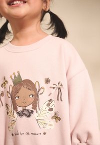 Rosa Sweatshirt mit einer Grafik eines Mädchens mit Schmetterlingsflügeln, gekrönt, umgeben von Blumen- und Insektenillustrationen, mit Bändchenakzenten.