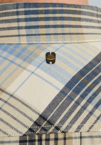 Chemise à carreaux beige et bleue avec une texture tissée, ornée d'une étiquette noire embossée "PME LEGEND" fixée au col.