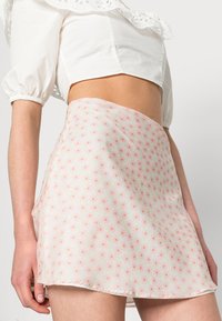Saia mini floral em tecido leve, com uma base rosa e padrões de flores multicoloridas subtis, com uma bainha crua.
