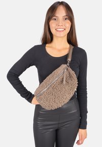 Braune, strukturierte, flauschige Umhängetasche mit Reißverschluss aus Silber und Lederriemen, die über einem schwarzen Oberteil getragen wird und ein lässiges Design zeigt.