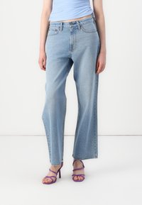 Jeans de pierna ancha de color azul claro, hechos de denim, con una cintura alta y una textura ligeramente desvanecida. Combinados con tacones morados con tiras.