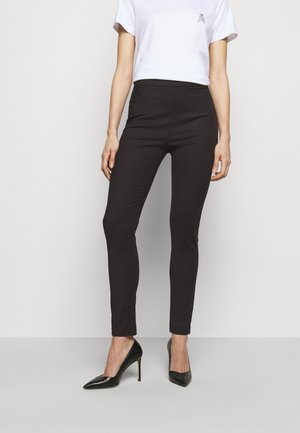 Sorte slim-fit bukser lavet af strækstof, med høj talje og elegant design, parret med spidse sorte hæle.