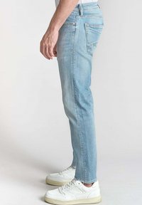 Jean en denim bleu clair avec une coupe droite, un style à cinq poches et un discret délavage. Associé à des baskets blanches.