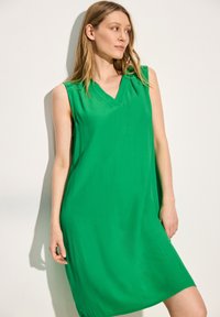 Robe verte sans manches avec un décolleté en V, fabriquée en tissu léger, dotée d'une coupe ample et d'une texture douce, arrivant au-dessus du genou.