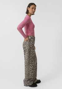 Top rosa ajustado de manga larga combinado con pantalones sueltos de estampado de leopardo que tienen bolsillos laterales y zapatos de plataforma negros planos.