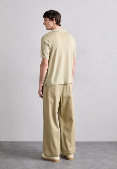 Ljusgrön kortärmad polo skjorta i kombination med lösa beige byxor och beige skor. Tyget verkar mjukt med en slät yta och minimal detaljering.
