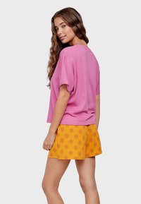 Roze oversized T-shirt met een ronde hals, gedragen met gele shorts met een zonnenpatroon. De stof lijkt zacht en casual.