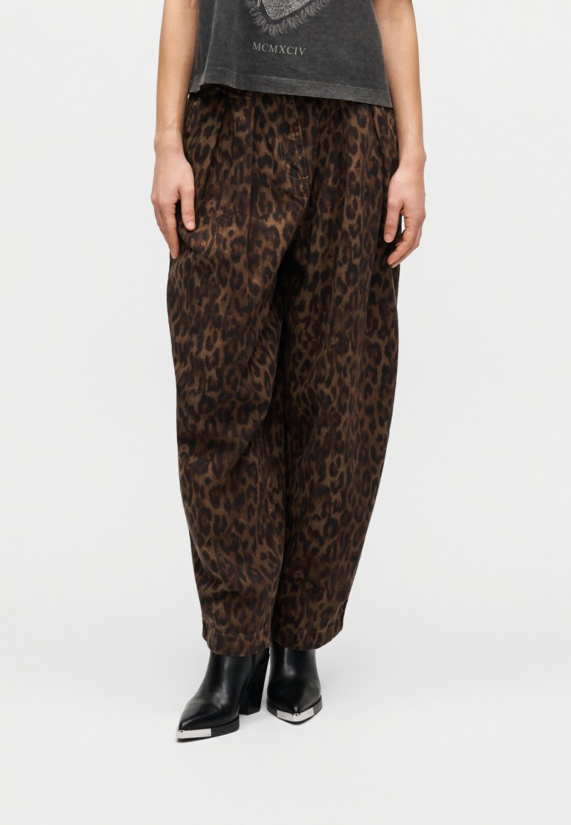 Παντελόνια φαρδιά με σχέδιο λεοπάρ σε καφέ και μαύρο ύφασμα. Διαθέτουν πιέτες για όγκο, συνδυασμένα με μαύρα μποτάκια αστραγάλου με μεταλλικές λεπτομέρειες.