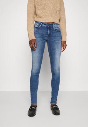 Jeans ajustados de color azul con un lavado desgastado, con bolsillos frontales y cierre de botón, combinados con un suéter de punto color beige claro.