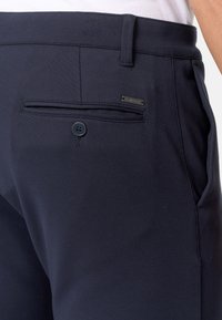 Pantalon bleu marine en tissu lisse, doté d'une poche arrière avec un bouton et d'une petite étiquette de marque, conçu avec une coupe classique.