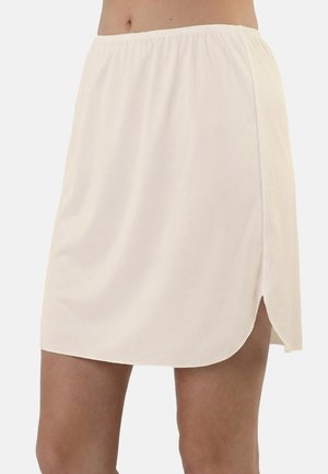 Cream-colored short skirt with elastic waistband and side slit worn by a person showing midriff and legs.
