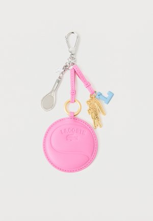 Llavero redondo rosa de Lacoste con un colgante de raqueta de tenis plateada, un colgante dorado de cocodrilo y una pequeña llave azul unidas a un clip metálico.