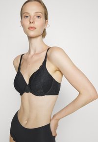 Black lace bra featuring adjustable straps, floral pattern, soft cups, and scalloped trim details, paired with high-waisted black briefs.