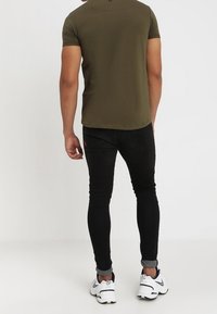 Olivově zelené upnuté tričko, černé skinny džíny s vybledlými akcenty, s manžetami u kotníků, v kombinaci s bílými teniskami.