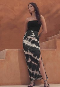Haut sans manches noir associé à une longue jupe avec un imprimé en tie-dye noir et blanc, une fente haute et des sandales plates avec des accents en chaîne.