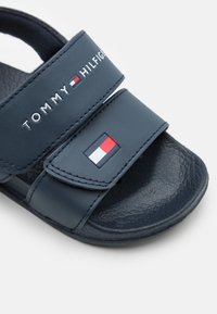 Sandalo a ciabatta blu navy con due cinturini regolabili, materiale testurizzato, con il logo "TOMMY HILFIGER" e un emblema a bandiera colorata.