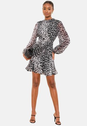 Schwarz-weiß gemustertes Kleid mit langen transparenten Ärmeln, tailliertem Schnitt, ausgestelltem Rock und rundem Ausschnitt; kombiniert mit einer schwarzen Clutch.