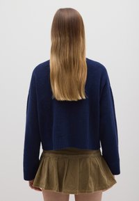 Maglione blu navy lavorato a maglia con orlo a coste e maniche lunghe, abbinato a una gonna plissettata in corduroy khaki. Tessuto morbido e vestibilità casual.