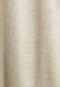 Gros plan sur un tissu en laine beige doux avec une texture tricotée fine, montrant des variations subtiles de couleur et des plis délicats.