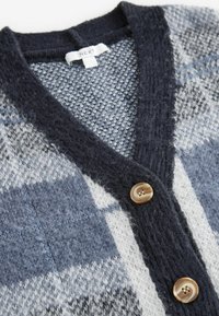 Cardigan à motifs bleu foncé et gris avec un col en V, présentant un tricot texturé et deux boutons beige clair près de l'encolure.