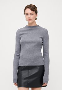 Grå ribbestrikket genser med lang erme, høy hals og hull for tommel, paret med et svart skinn miniskjørt. Glatt tekstur, tettsittende design.
